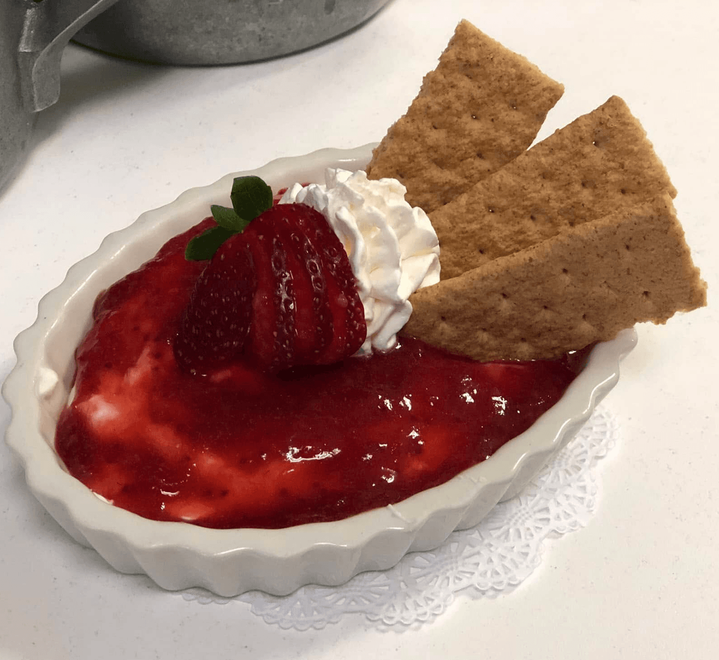 A small dish of strawberry dessert topped with whipped cream, a fresh strawberry, and graham cracker pieces.