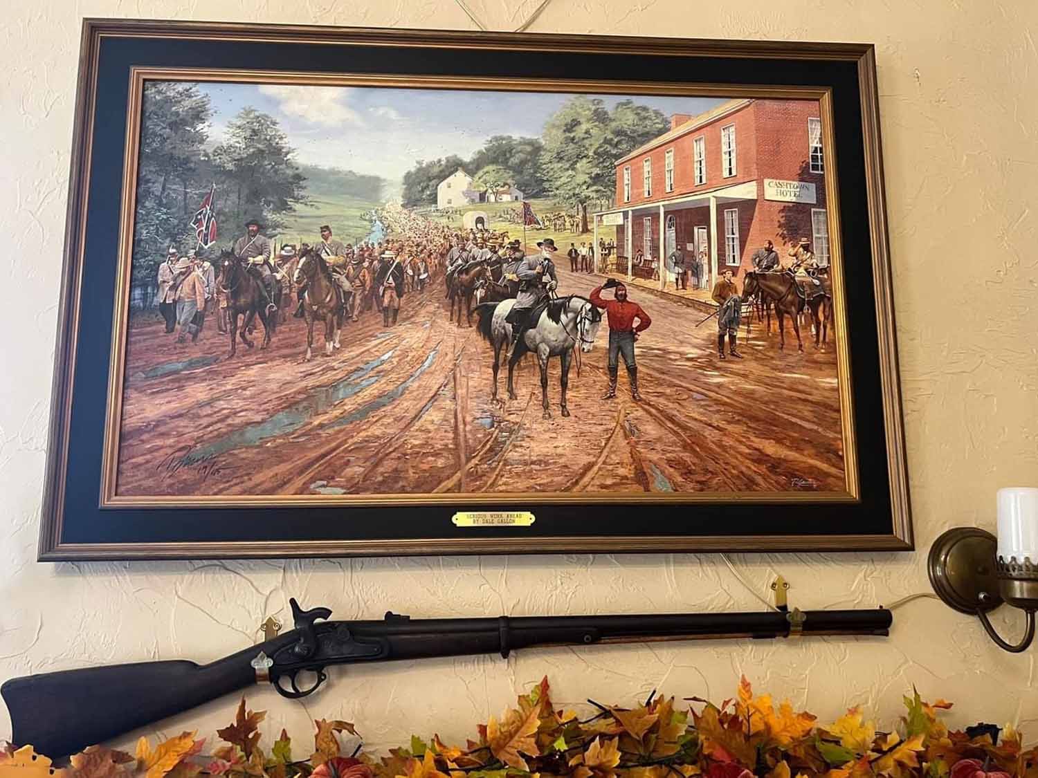 A framed painting depicting a historical cavalry scene on a muddy road, accompanied by a vintage rifle displayed below.