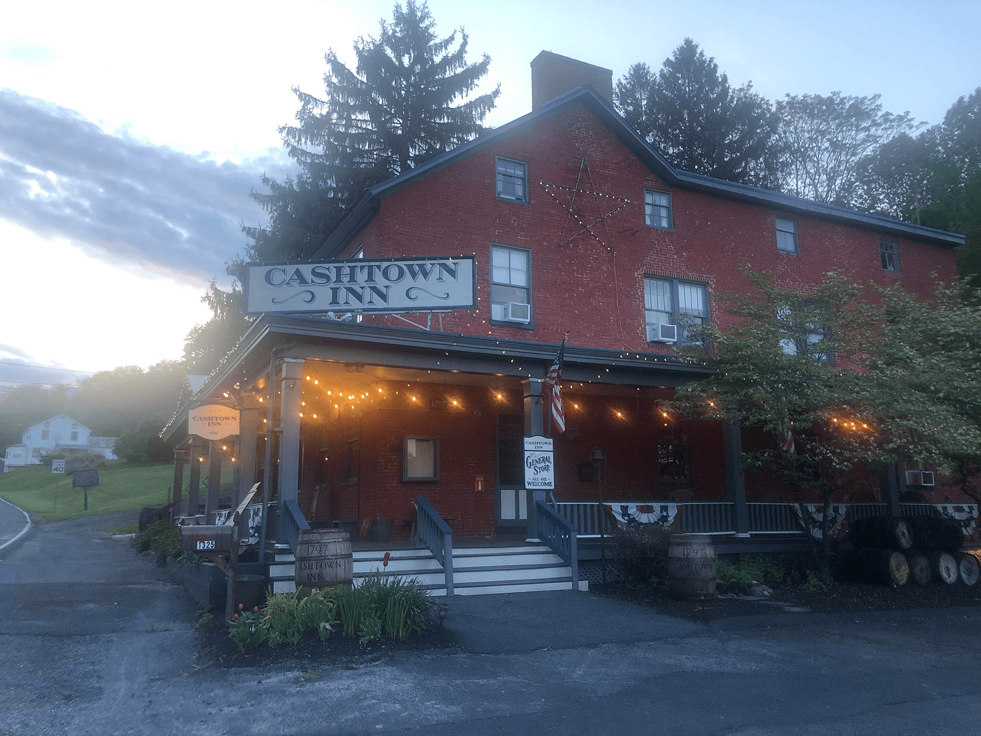 A brick inn with a sign reading "Cashtown Inn" is illuminated by string lights at dusk.